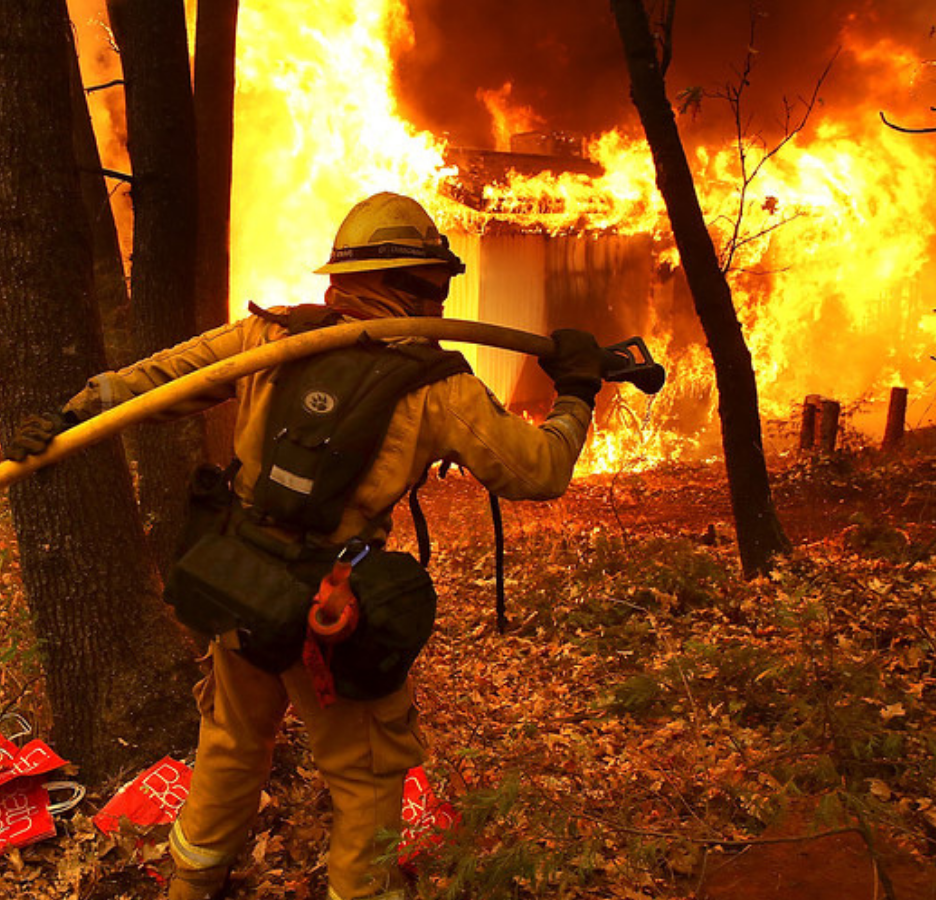 fireman with a hose standing in front of a burning house